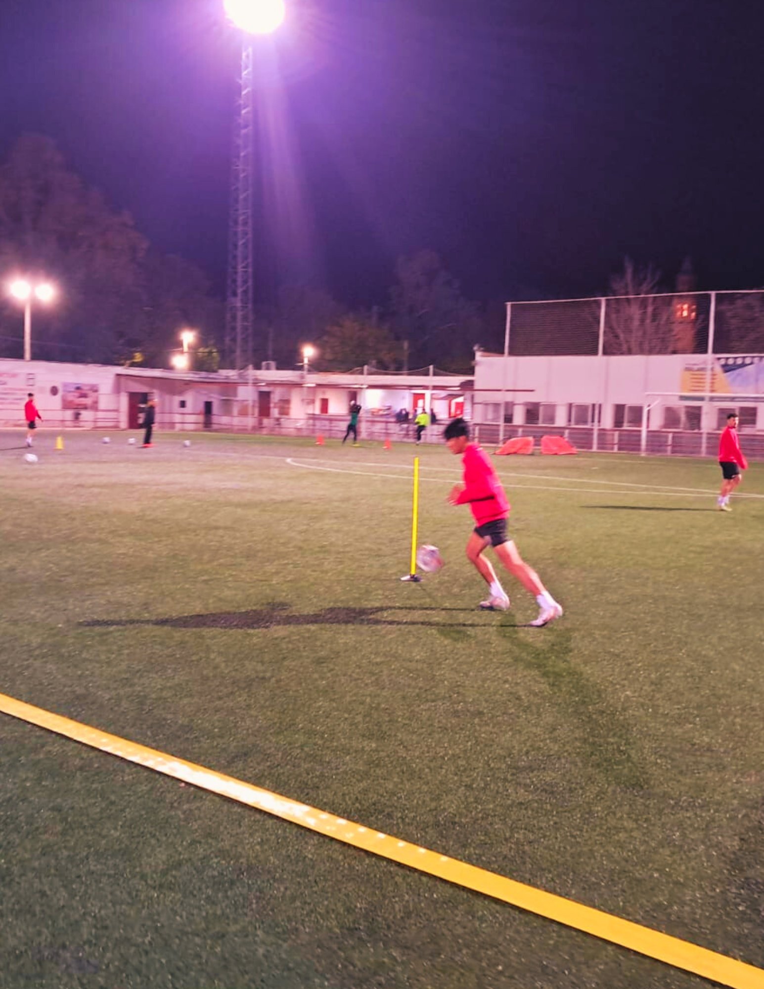 Leo Avalos practicing soccer drills on a professional field in Spain, wearing a red training top and showcasing his dedication to skill development.